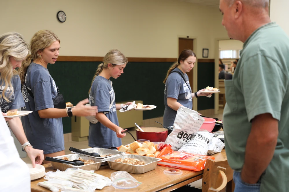 Young women in line at a table filling plates with food.